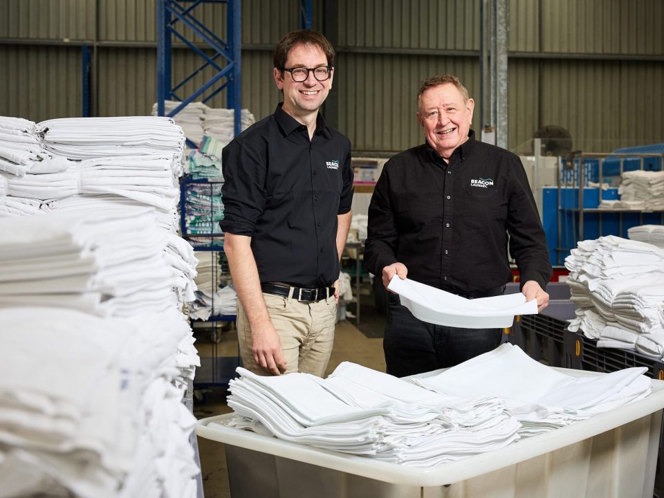 Two men in dark shirts with Beacon logo standing in a laundry