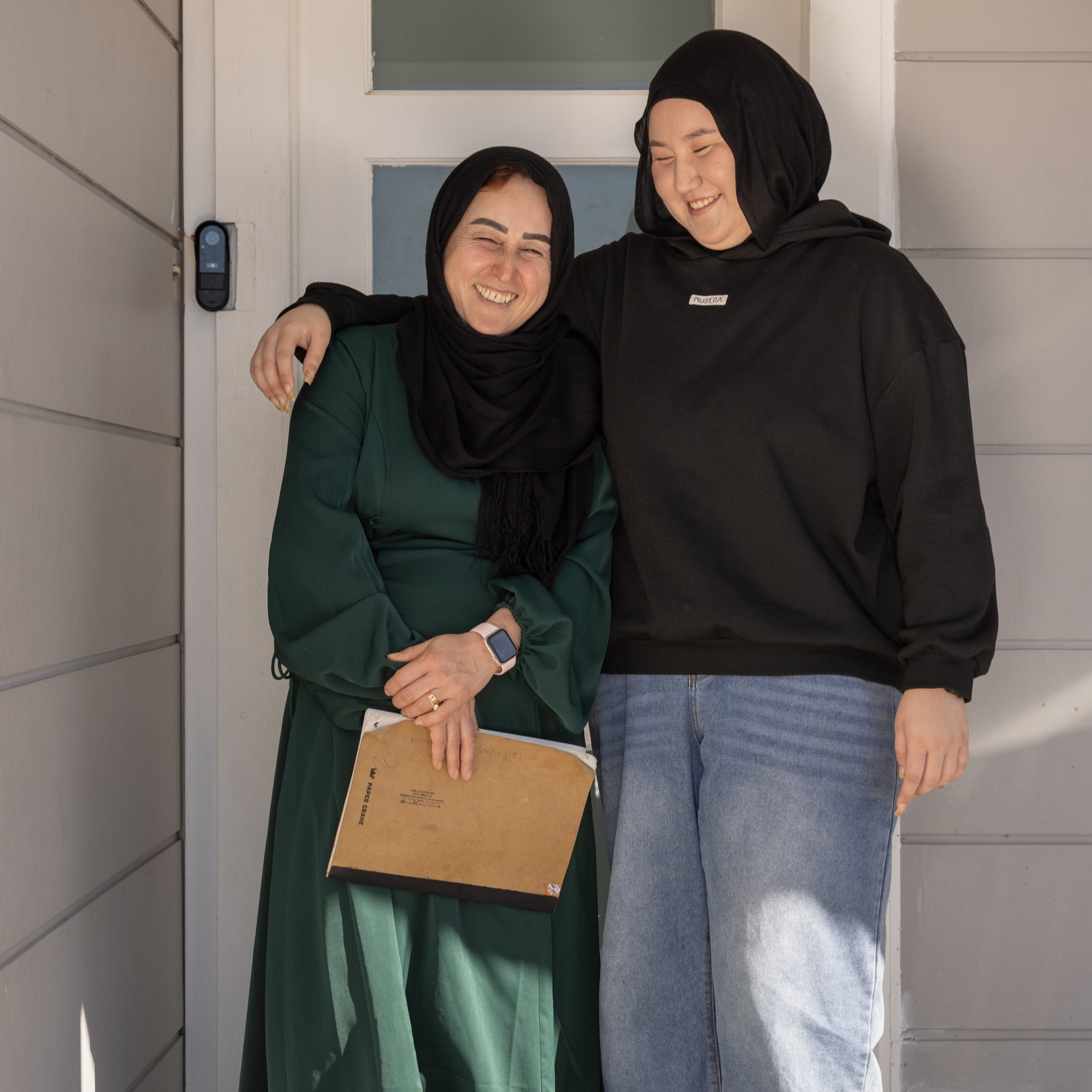 A mother and daughter standing together, smiling at their front door.
