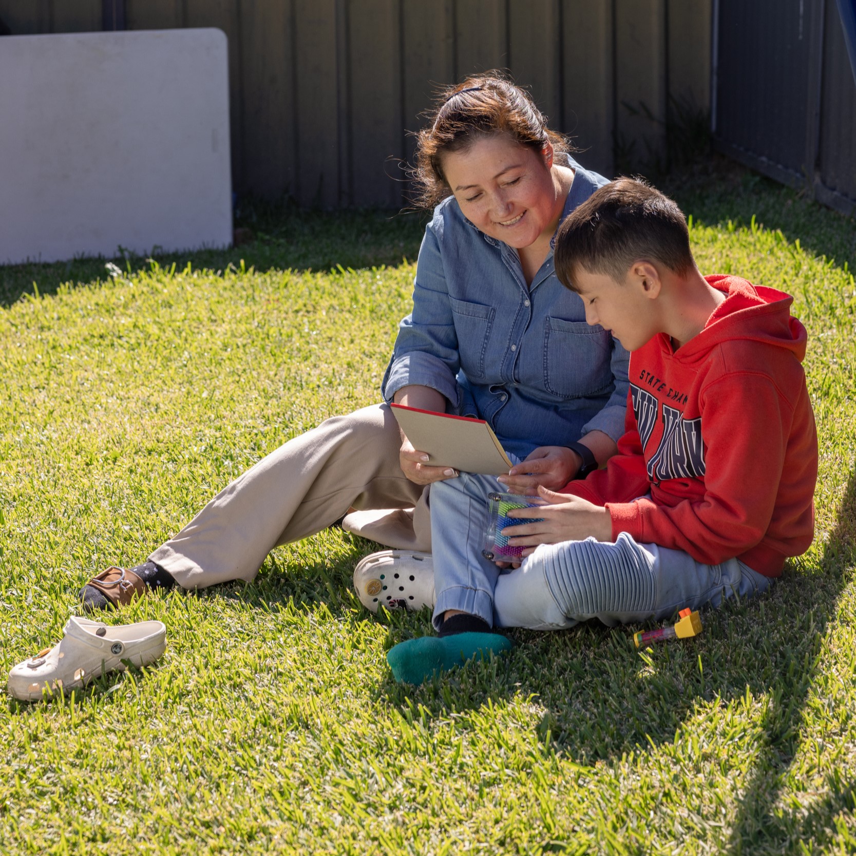 A mother sitting with her young boy in the backyard, reading a letter.